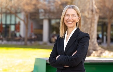 Headshot of Center Director Cinnamon Bloss wearing a Navy Suit with her arms crossed, standing on the campus quad